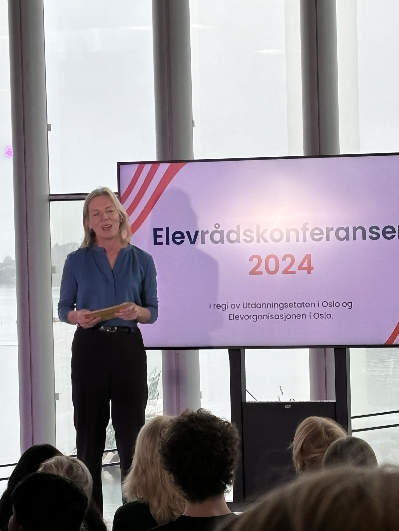 en person som står foran en skjerm med en gruppe mennesker som sitter