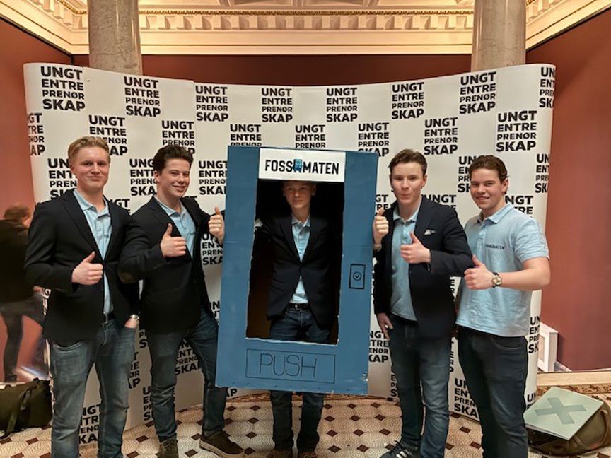 En gruppe menn poserer for et bilde foran et skilt