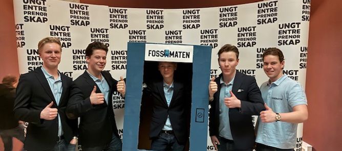 Foto: Foss vgs, Ungdomsbedriften Fossomaten En gruppe menn poserer for et bilde foran et skilt