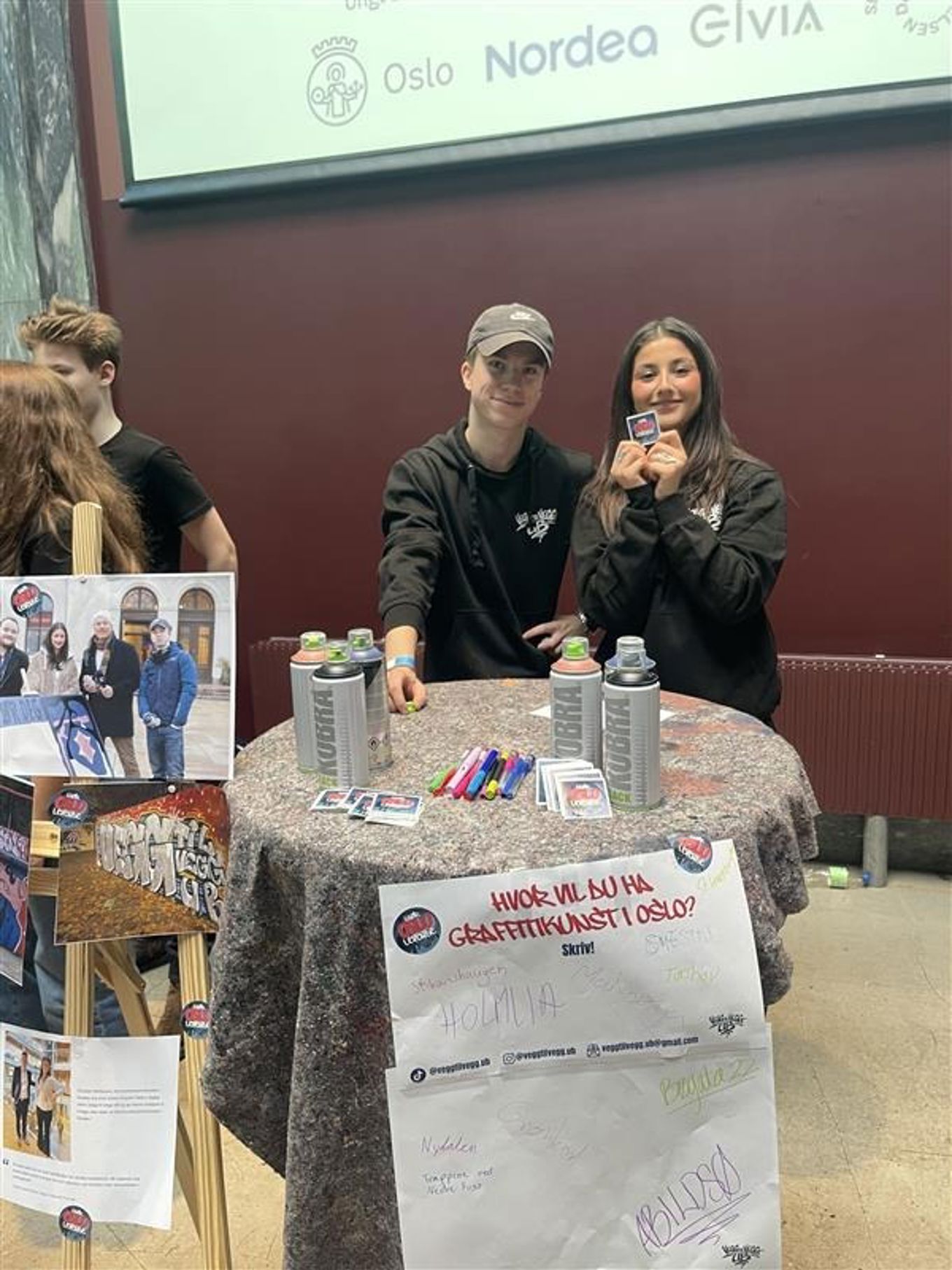 Foto: Foss vgs en person og en person som står bak et bord med et skilt og en flaske vann