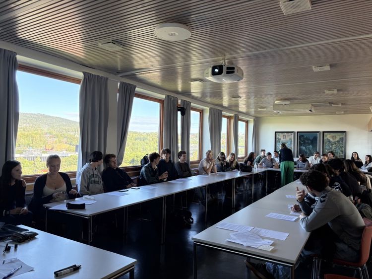 en gruppe mennesker som sitter ved langbord i et rom med vinduer
